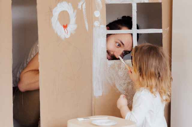 bambina pittura una parete di cartone mentre il padre la guarda